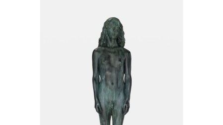 Sculpture of a nude woman above a pedestal reading 'WOMAN'. The sculpture's material is distressed so that it appears to have been worn down over time.