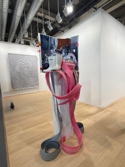 A sculpture with a white pedestal in which several things are piled on including a pair of white boots.