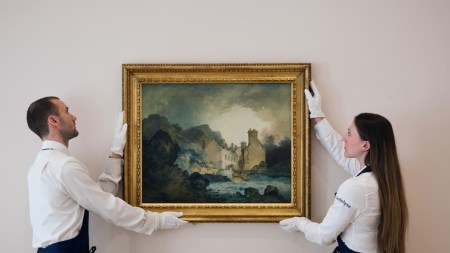 Two white gloved art handlers hold a rediscovered landscape by J.M.W. Turner.